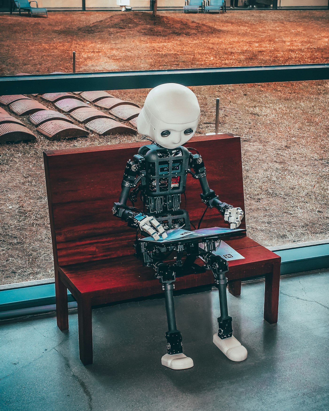 A humanoid robot sitting on a bench reading, a visual metaphor for AI assistants acting as advisors